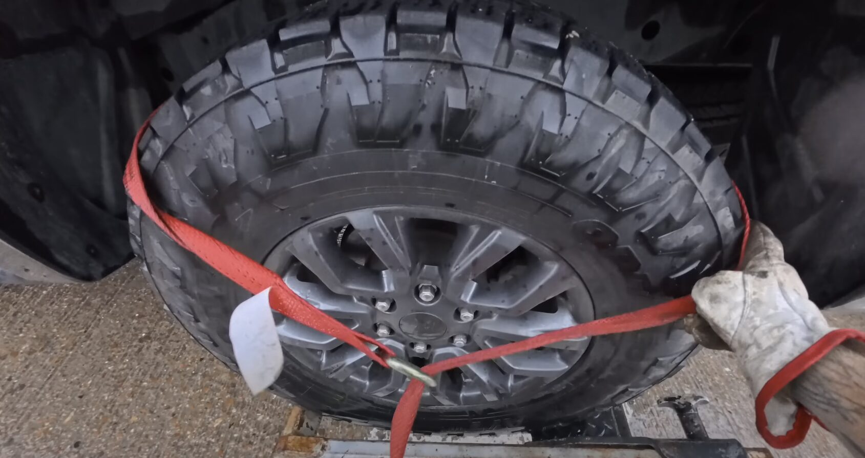 Damaged tire secured with red straps on tow truck platform